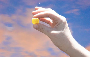 Hand holding a Delta 9 THC Indica gummy in the sky