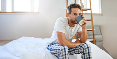 A man sitting in bed drinking from a mug