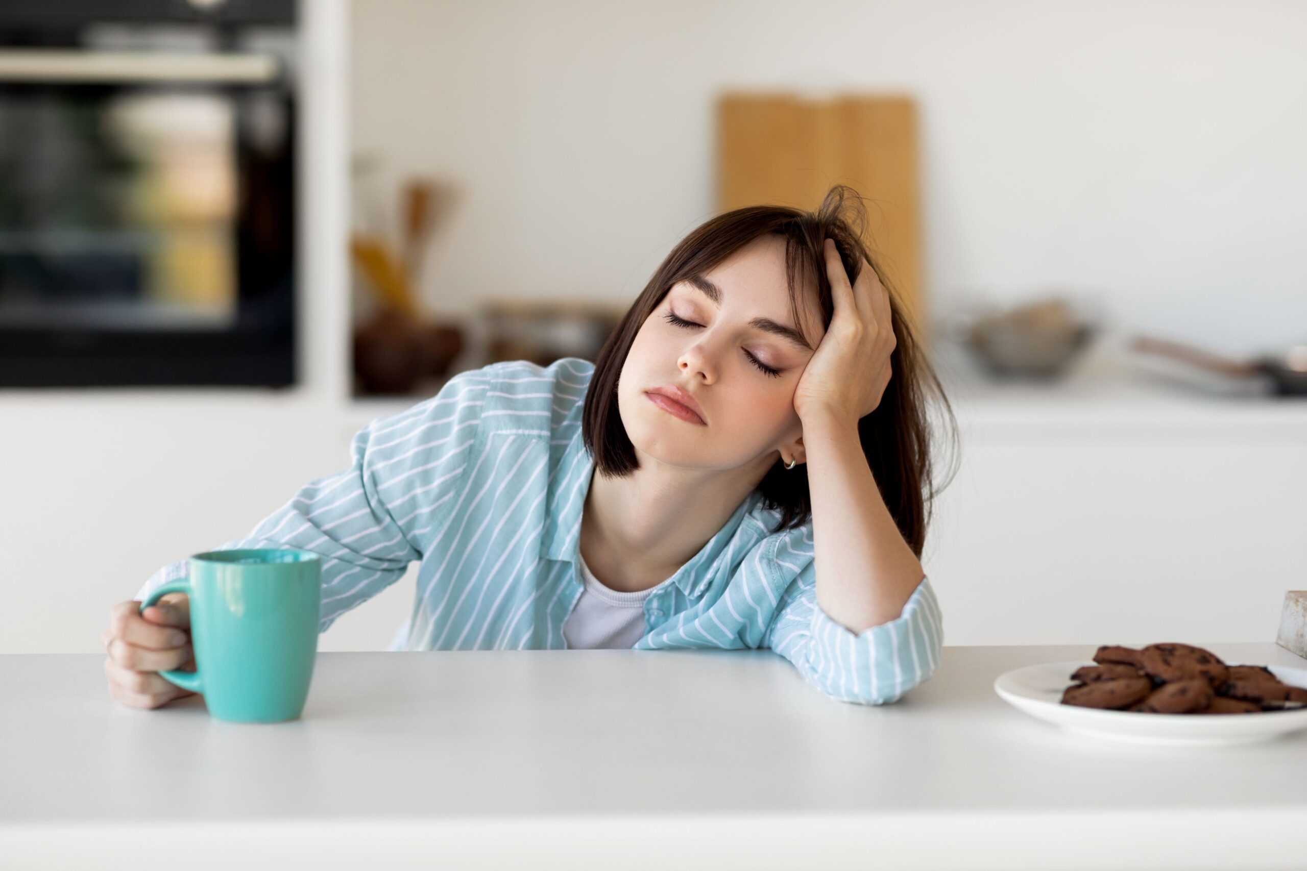 Woman sitting at a table falling asleep with coffee mug in her hand