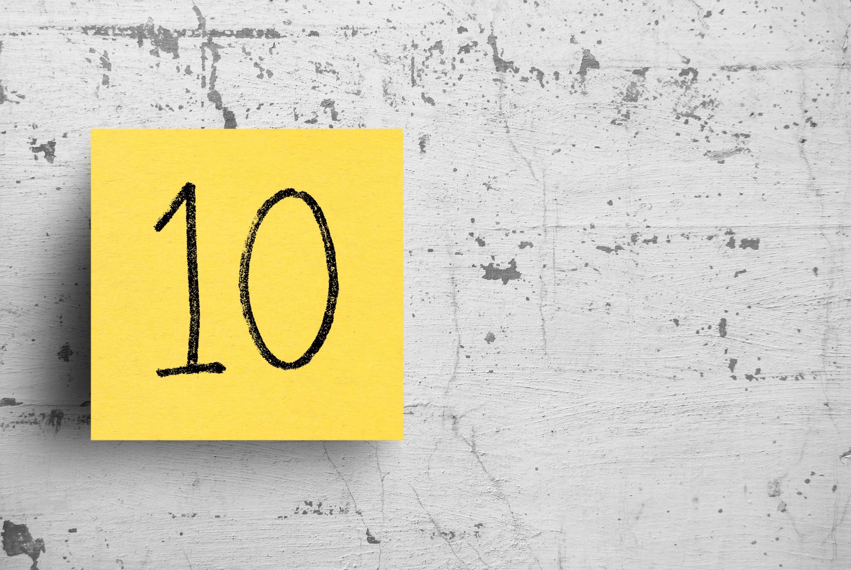 The number 10 written on a yellow sticky note hanging on brick wall