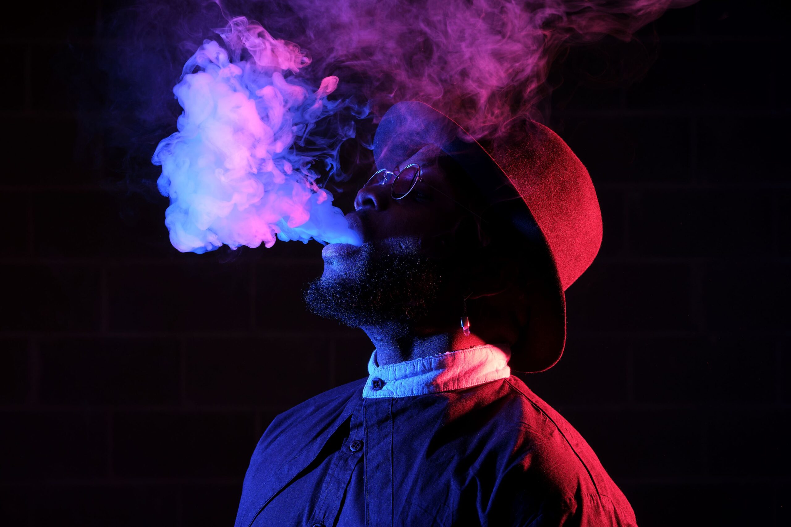 Man blowing smoke cloud upwards in red, blue, and purple lighting