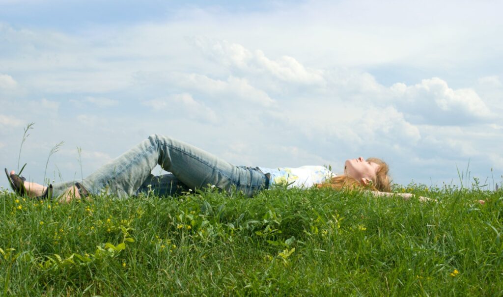 Girl laying in the grass during the day watching the clouds