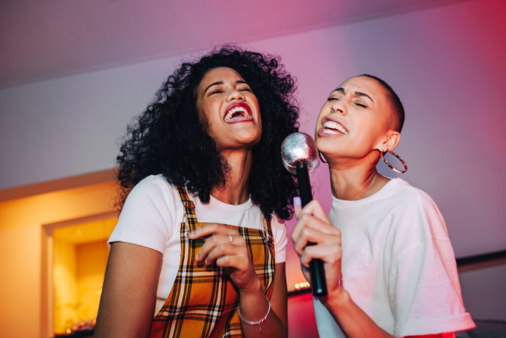Two women sharing a microphone happily singing karaoke
