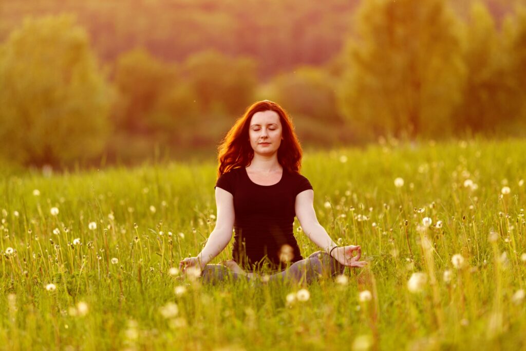 Woman therapeutically meditating in a grass field
