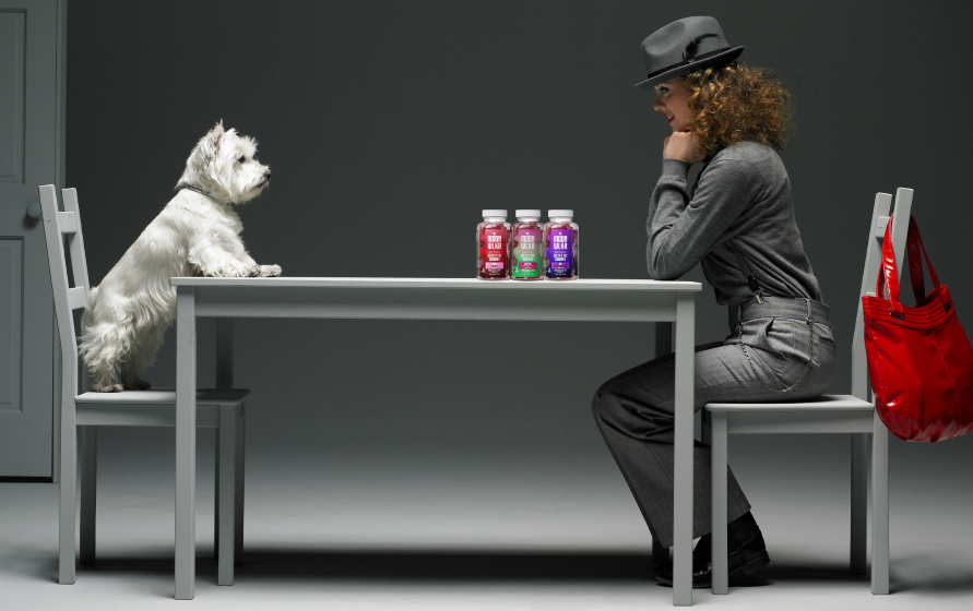 Dog and woman sitting at either ends of a table with bottles of Delta-9 gummies on it