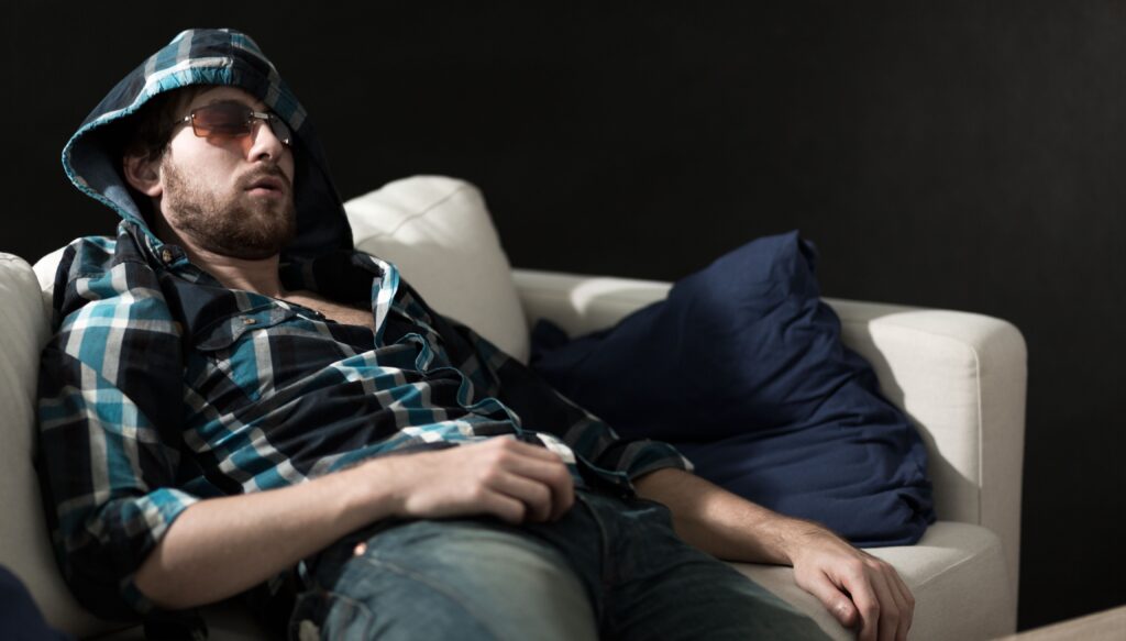 Man passed out asleep on a couch with hood up and sunglasses on