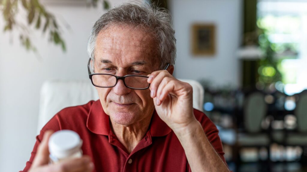 A man holding his reading glasses to his face while observing the product label on a bottle