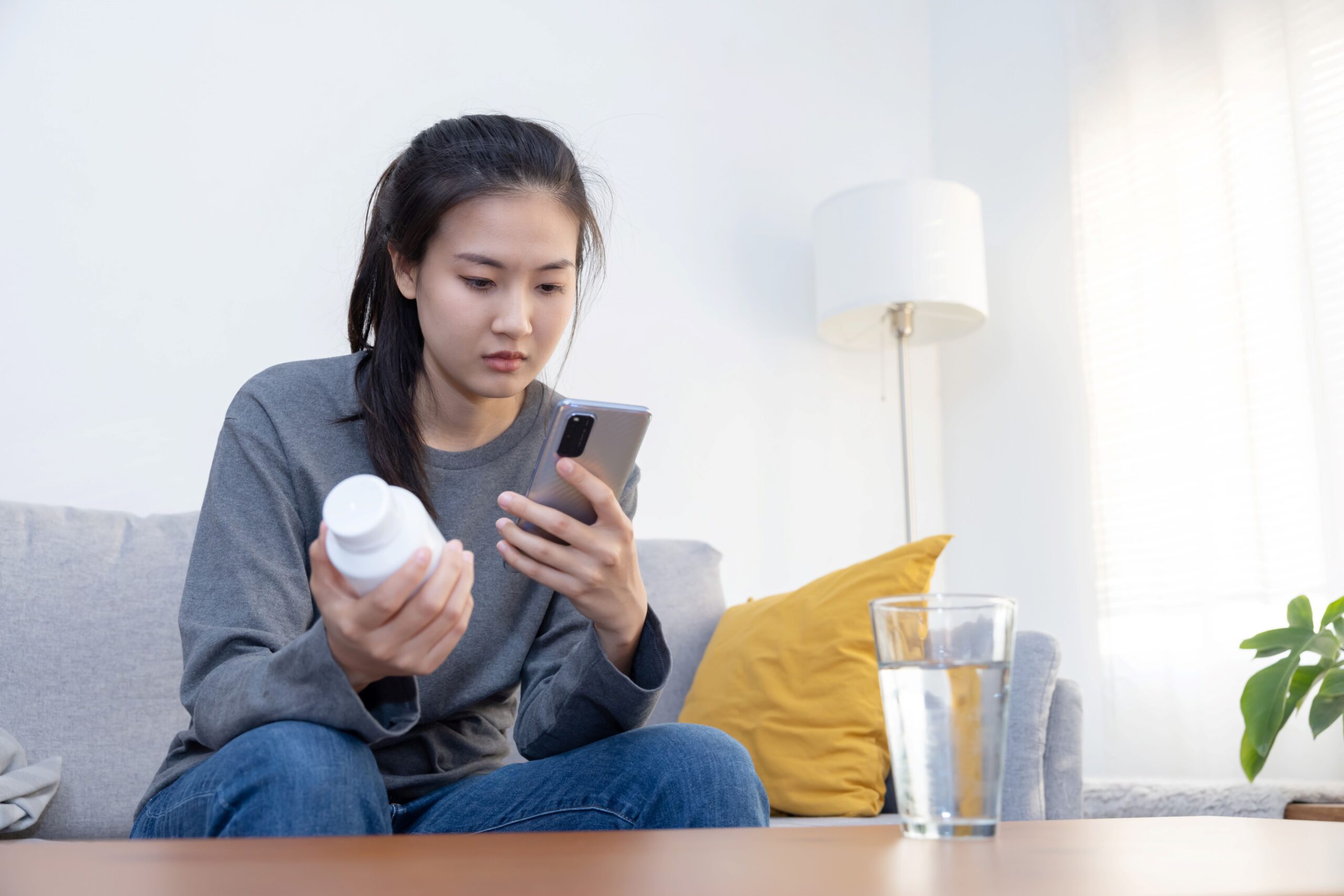 Woman sitting on couch with product bottle looking up information on her phone