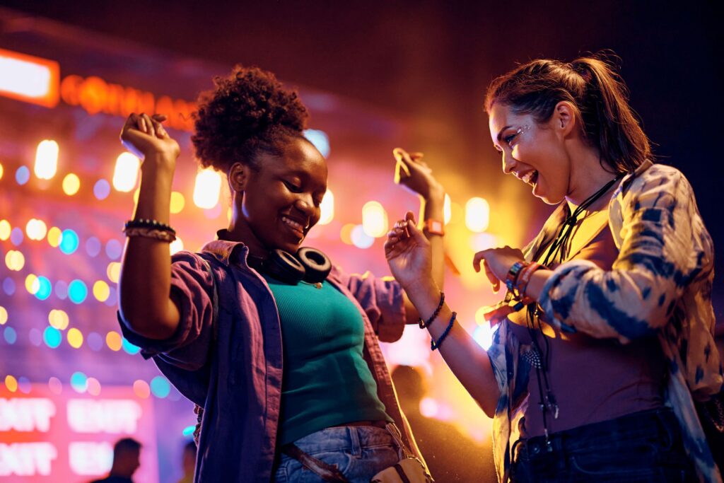 Two friends dancing together in front of concert lights