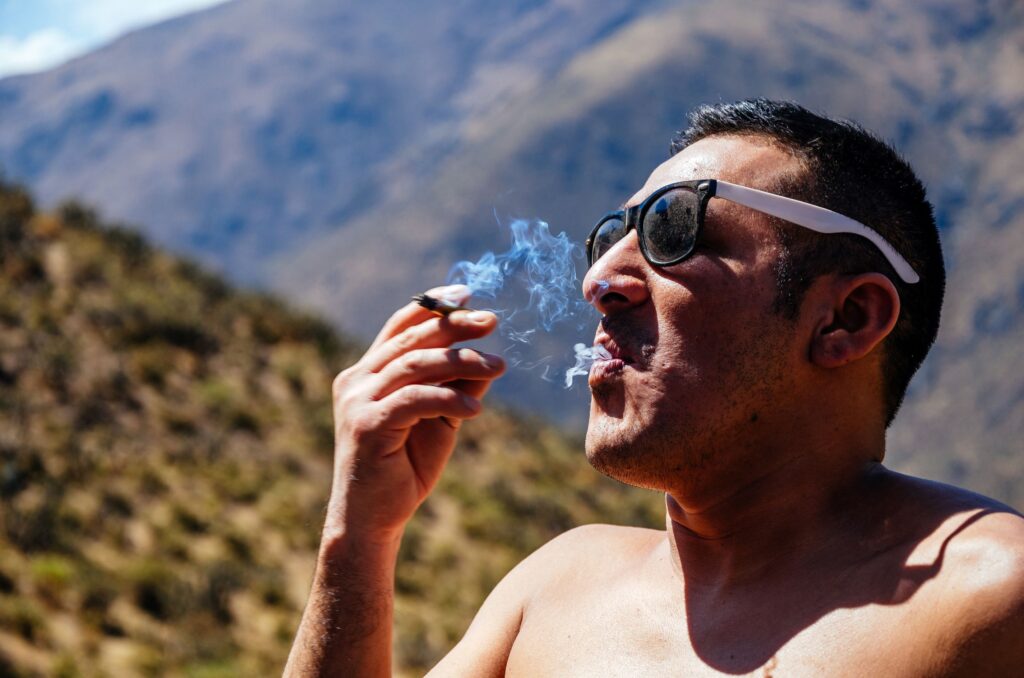 A man wearing sunglasses out in the mountains smoking a pre-roll