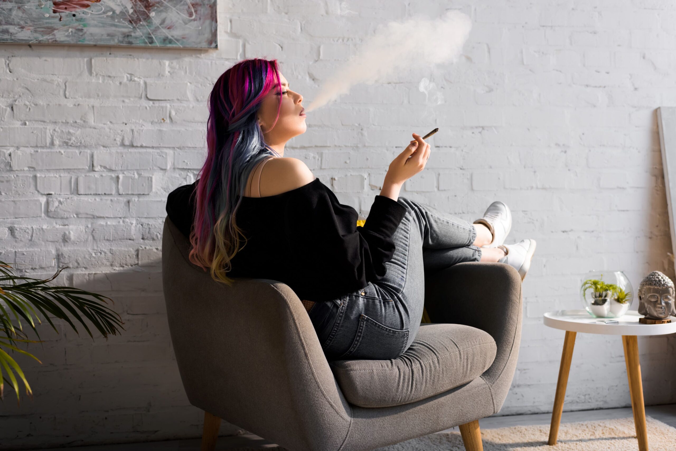 A woman lounging in a chair while blowing smoke from a joint